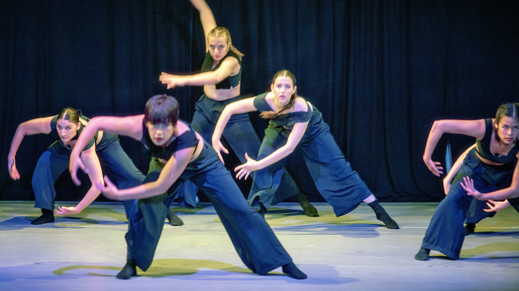 Five dancers leaning over, swinging their arms while looking intently ahead.